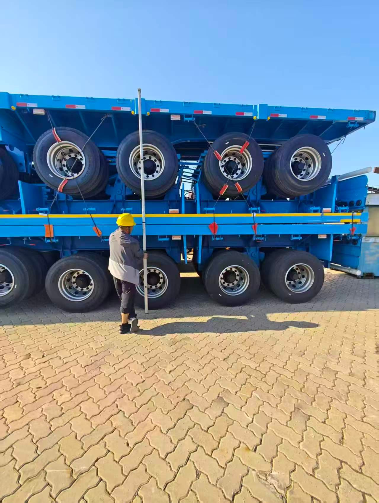 Worker measuring and inspecting stacked blue semi-trailers before export shipment