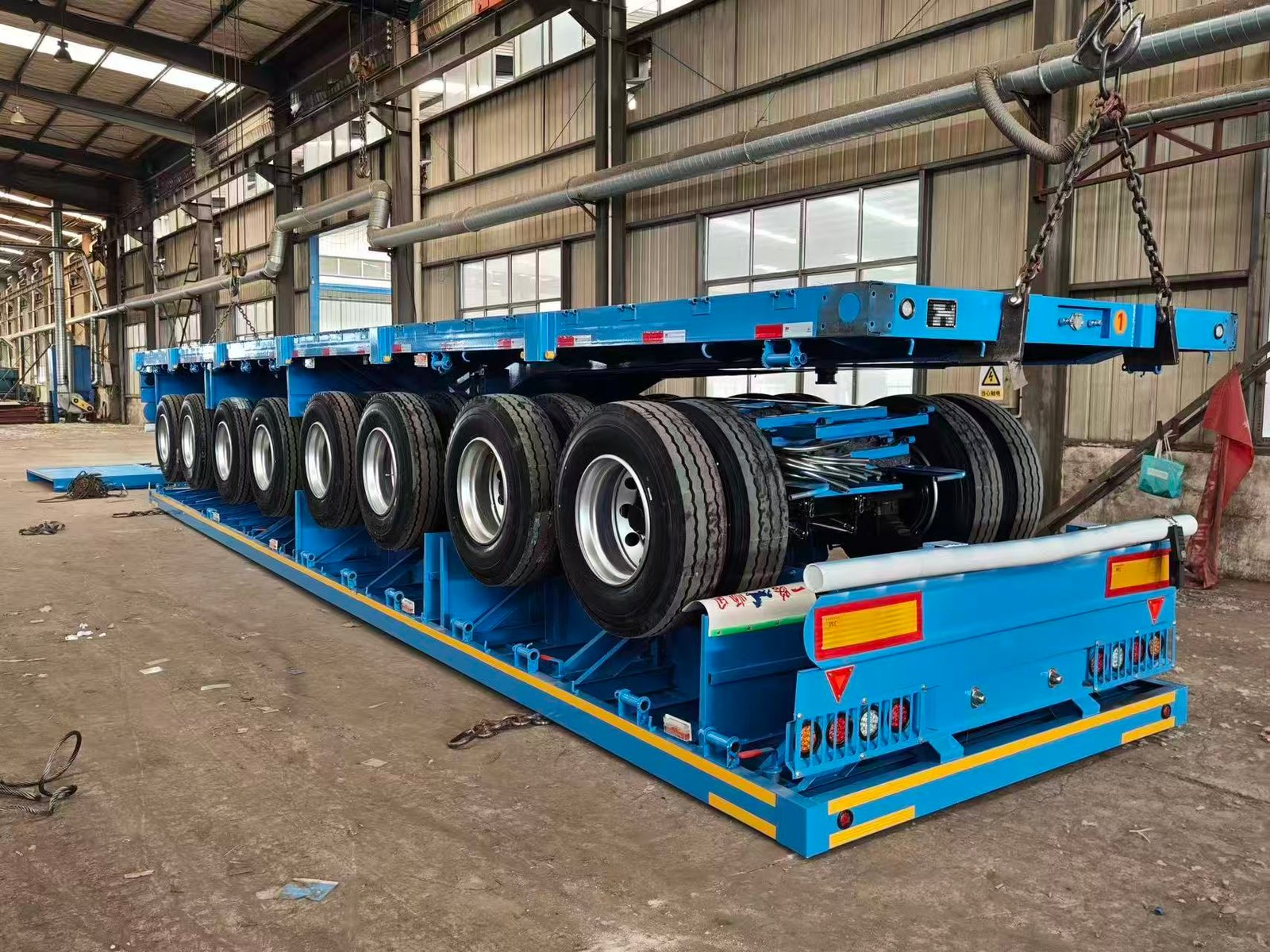 Blue multi-axle semi-trailer being assembled and prepared inside a vehicle workshop in China